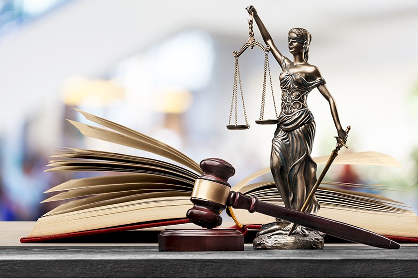 Justitia Statue mit Richterhammer und Buch auf einem Tisch