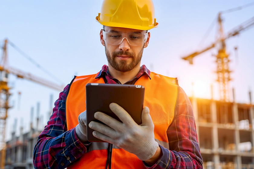 Mann auf Baustelle mit Helm, Schutzbrille und Tablet in der Hand
